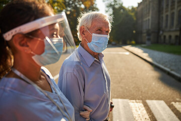 Handsome elderly man in protective mask spending time with medicine worker in the city