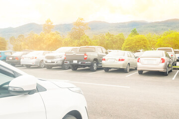 Fototapeta na wymiar Car parked in large asphalt parking lot with trees, cloudy sky and mountain background. Outdoor parking lot with fresh ozone and green environment of travel transportation concept
