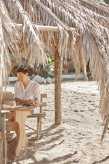 Young woman using laptop computer on a beach. Freelance work concept..Pretty young woman using laptop in cafe on tropical beach in outdoor cafe. Work and travel
