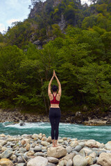 Yoga classes in nature. The concept of playing sports alone. Social exclusion. A woman does yoga on rocks, near a mountain river flows