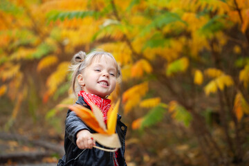 Happy smiling blonde girl holding yellow red leaves in sunny autumn park