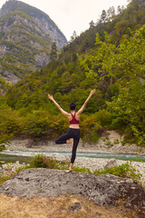 Yoga classes in nature. The concept of playing sports alone. Social exclusion. A woman does yoga on rocks, near a mountain river flows