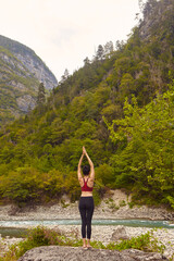 Naklejka premium Yoga classes in nature. The concept of playing sports alone. Social exclusion. A woman does yoga on rocks, near a mountain river flows