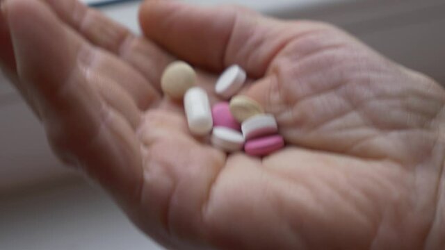 Moving shot of wrinkled senior hand shaking pills. Different color medicine tablets in one shot.