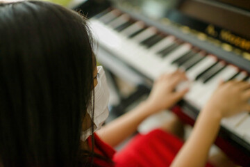 Pretty young musician playing upright piano at home during online class, social distance during quarantine, self-isolation, online education concept.Female Asian plays instrument.