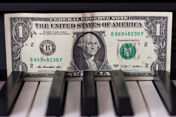 One dollar banknote lying on the piano keys. The dollar as a symbol of global economic management.