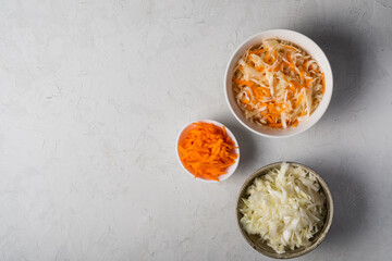Cabbage and carrots are chopped and prepared for pickling in three bowls on a gray background. The best natural probiotic. Fermented product