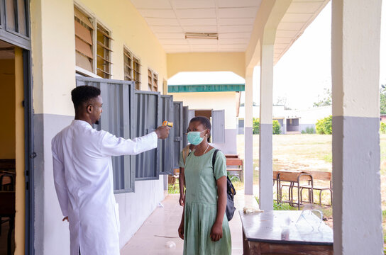 a young handsome african class teacher holding as thermometer to scan the temperature of his student before entering the classroom - Powered by Adobe