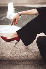 Female hand and leg in black pants and velvet red shoes. Street style fashion details