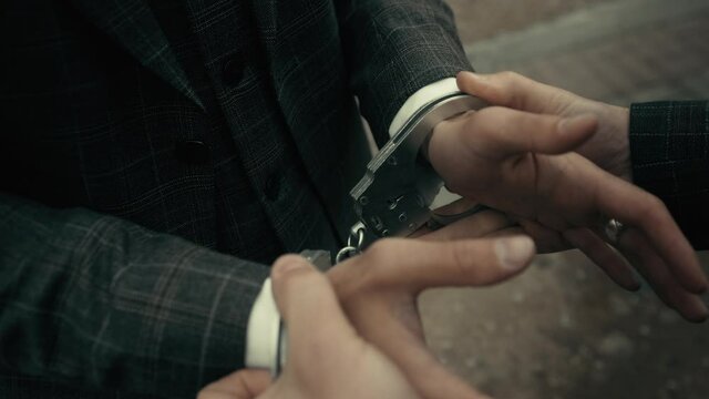 Arrest of the offender without resistance. Policeman puts the handcuffs on the hands of criminal, hands closeup. Detention of the accused business person.