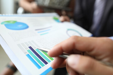 Male hand holds ballpoint pen over document with graphs and charts in office closeup. Development...
