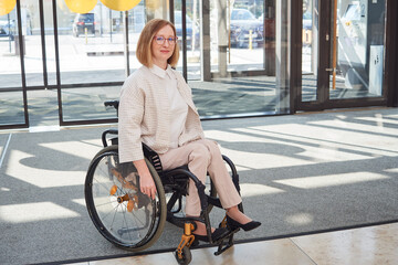 adult woman in wheelchair enters the mall through glass doors. The concept of accessible environment