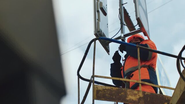 A worker in the elevator cradle fixes the LED traffic light. Medium shot. LED technology. Road sign.