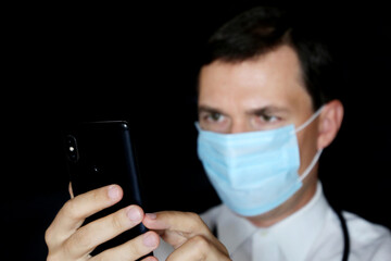 Doctor in mask using smartphone, mobile phone in male hand close up. Concept of appointment online, medical exam