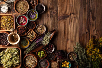 Fototapeta na wymiar Natural medicine theme. Assorted dry herbs in bowls and brass mortar on rustic wooden table.