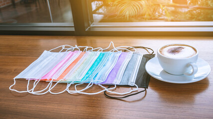 Colorful of surgical masks for Coronavirus(Covid-19) protection with hot cappuccino coffee for those in quarantine areas on wooden table. Beautiful multicolored masks. Selective focus