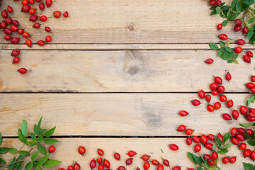 Rose hip, rosa canina, on the wooden table with copy space in the middle. Red berries on side of the brown board with woody pattern. Fresh little fruit on the top of the palette with space for text.