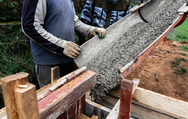The concrete mixer loads the concrete through a chute into a timber formwork with metal reinforcement to create a solid foundation for a building or fence. Construction process