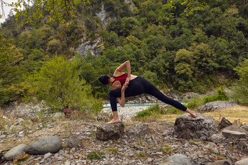 Yoga classes in nature. The concept of playing sports alone. Social exclusion. A woman does yoga on rocks, near a mountain river flows