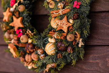 Traditional Christmas wreath made of fir branches, decorated with ginger cookies, cinnamon, nuts, berries, bells and a beautiful bow © Lena May