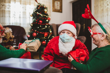 Cute boy with his grandparents wearing facemask while celebrating Christmas at home during the COVID-19 pandemic