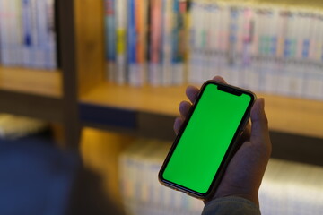 over shoulder view of people holding green screen smart phone in library. Defocused books on...
