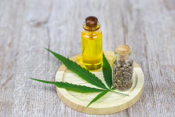 CBD hemp oil, aside tea, and cannabis leaves are placed on a wooden plate.Medical ideas research hemp leaves and hemp oil using the oil as a therapeutic herb.