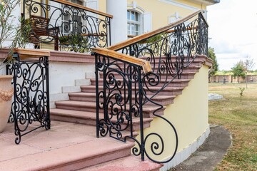 Fragment of a porch with black forged railings and a gate, descent from the terrace to the park