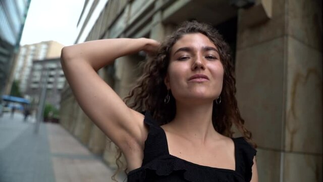 a young woman with curly hair poses on a city street. camera zooms in