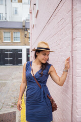 Woman in Blue Dress Has a Reflexive Look as she Touches a Pink Wall