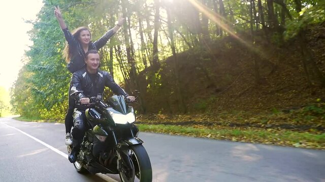 young happy couple in love motorcyclists in black leather jackets on a sports bike ride on the road smiling and hugging. Young sexy woman with boyfriend drive. Lifestyle. through the woods and trees