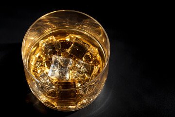 Glass of whiskey with ice on a black background. Top view.