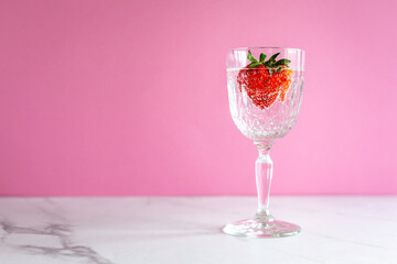 A single glass with a strawberry with bubbles on pink background and marble surface, horizontal