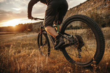 Crop man riding mountain bicycle at sunset