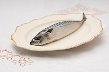 Old decorative presentationdish with tasty raw mackerel fish on table with an embroidered tablecloth