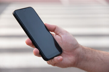 Man's hand holding a smart phone in the street