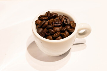 Cup with roasted coffee beans on white background. Copy space 