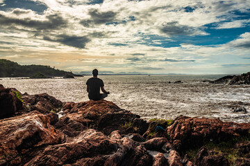 man meditating at rock at sea shore at morning from flat angle