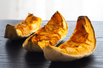 Roasted pumpkin slices. Freshly baked and juicy slices of pumpkin on the black table. Autumn flavors. Simple food concept. Baked in the oven. Healthy vegetarian food. 