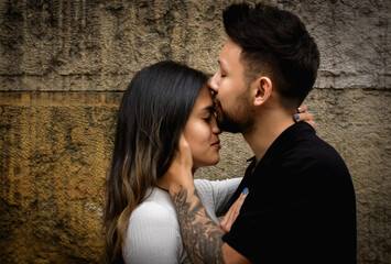 hombre joven dando un beso a su novia en la frente  con una pared rustica desgastada en el fondo 