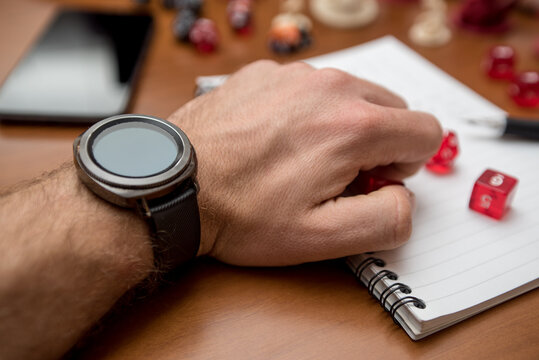 Man wearing a smartwatch ready to play role game like dungeons and dragons with the dices, smartphone and dices. - Powered by Adobe