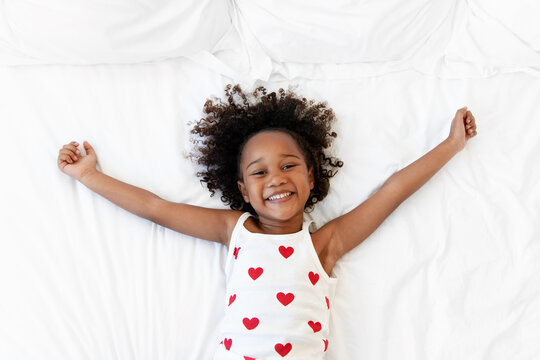 Happy little girl lying on bed with arms extended