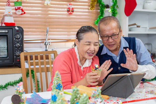 Senior An Asian grandfather and grandmother wearing aprons learning to make cupcake online with a tablet having fun in a kitchen.