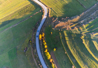 Drone view, passing cars on asphalt road trough agricultural fields at autumn.