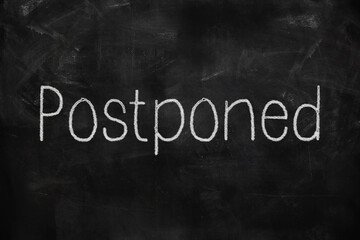 Postponed written with white and red chalk on blackboard