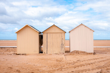 Three beach huts at the coast of Ouistreham, France, with blue sky with clouds