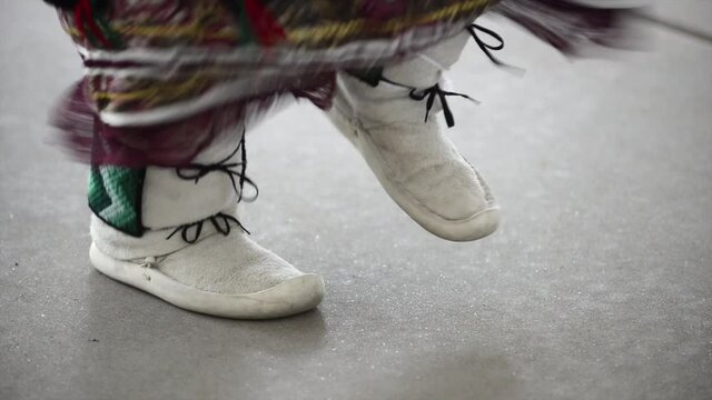 Native American dancer in moccasins dances to drum beat.