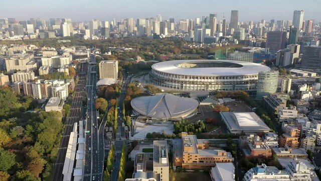 A spinning 4k drone shot of the Tokyo city area featuring two olympic venues in the foreground, the Tokyo Metropolitan Gymnasium and the Japan National Stadium and the larger Tokyo skyline.