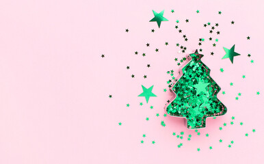 Christmas tree made of cookie form and green confetti at pastel pink background. Creative festive decoration concept.