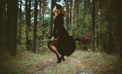 Young beautiful and mysterious Witch woman Flying on the Broom in woods. Levitation, a witch on a broom, free space. Halloween holiday, magic